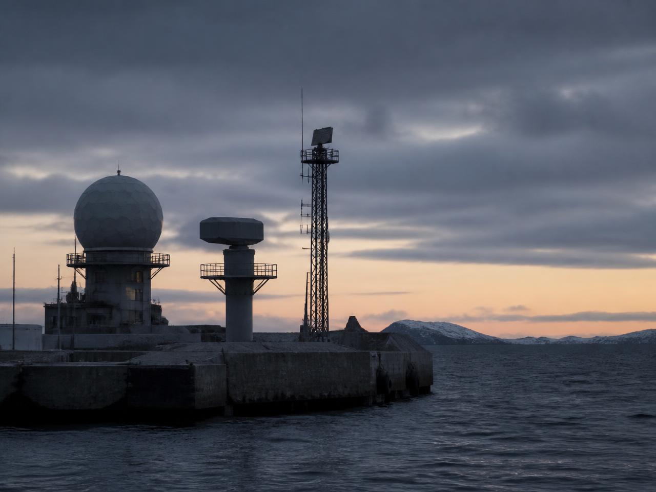 Coastal defence site with radar domes and sensor masts on a quay at twilight